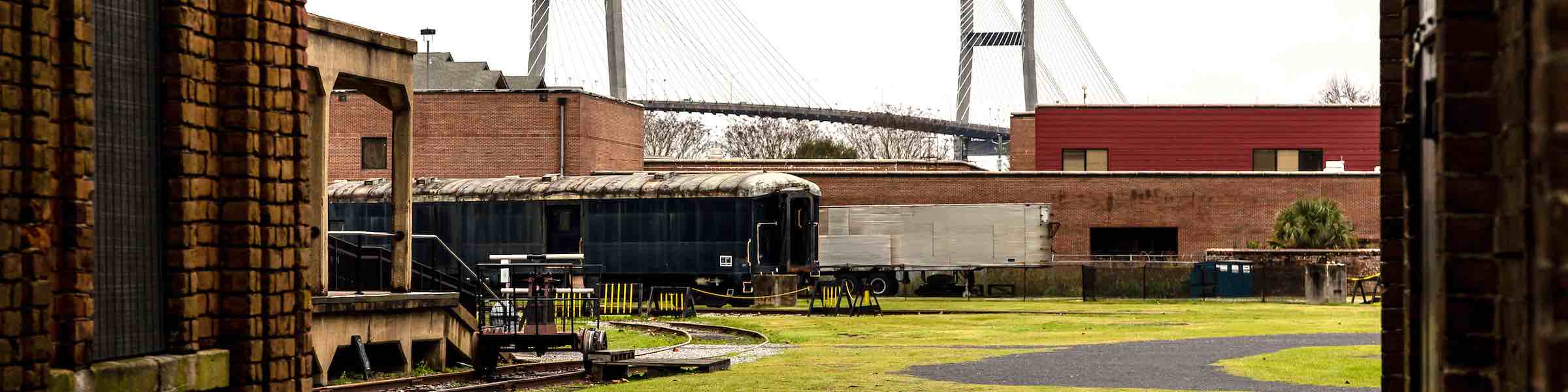 A train seen through an archway at the Georgia State Railroad Museum, Savannah, GA. In the background is the Savannah River Bridge.