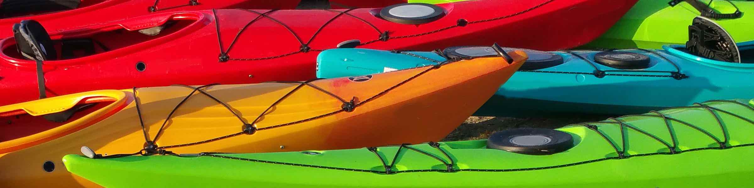 Several colorful kayaks pulled up together on a beach.