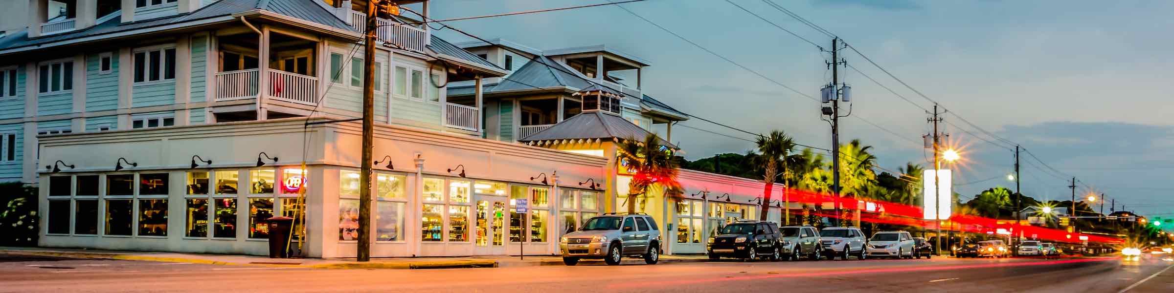 Dusk scene along Butler Avenue, Tybee Island, showing a brightly lit store front and streaks of light from passing vehicles.